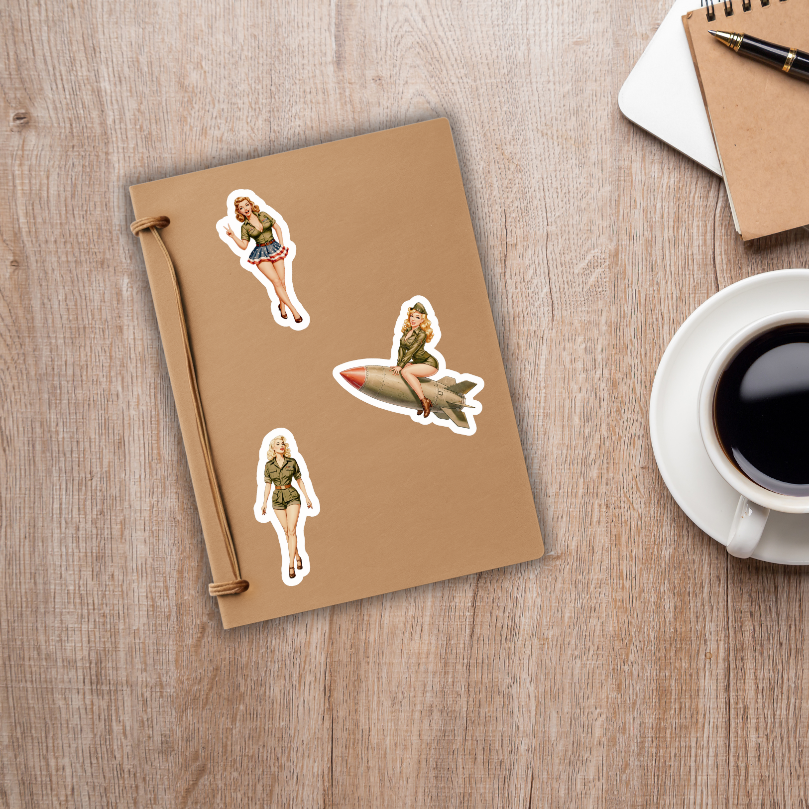Notebook with stickers of a woman on a surfboard and a rocket, next to a cup of coffee on a wooden surface.