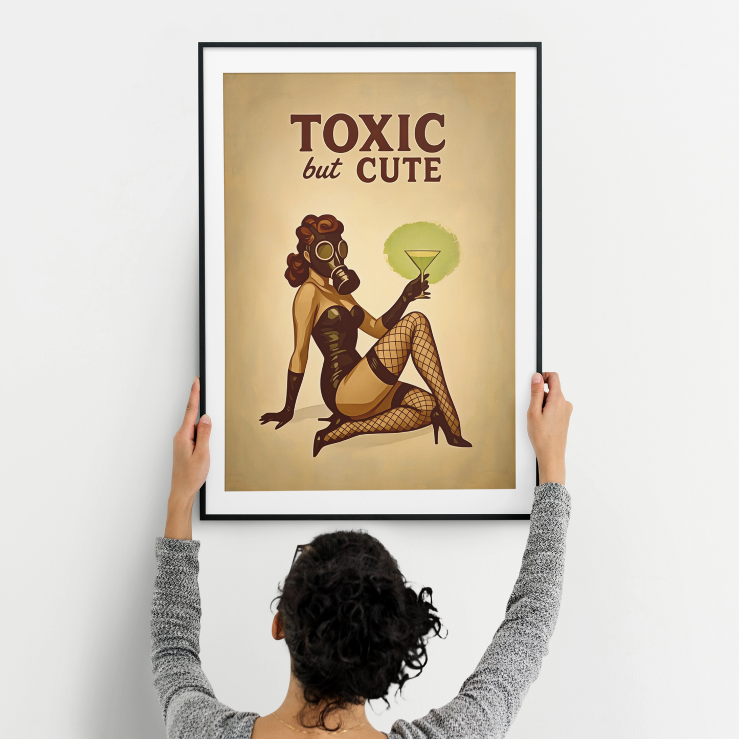 Person hanging a framed poster with a stylized illustration of a woman in a gas mask and text 'Toxic but Cute' on a beige background.
