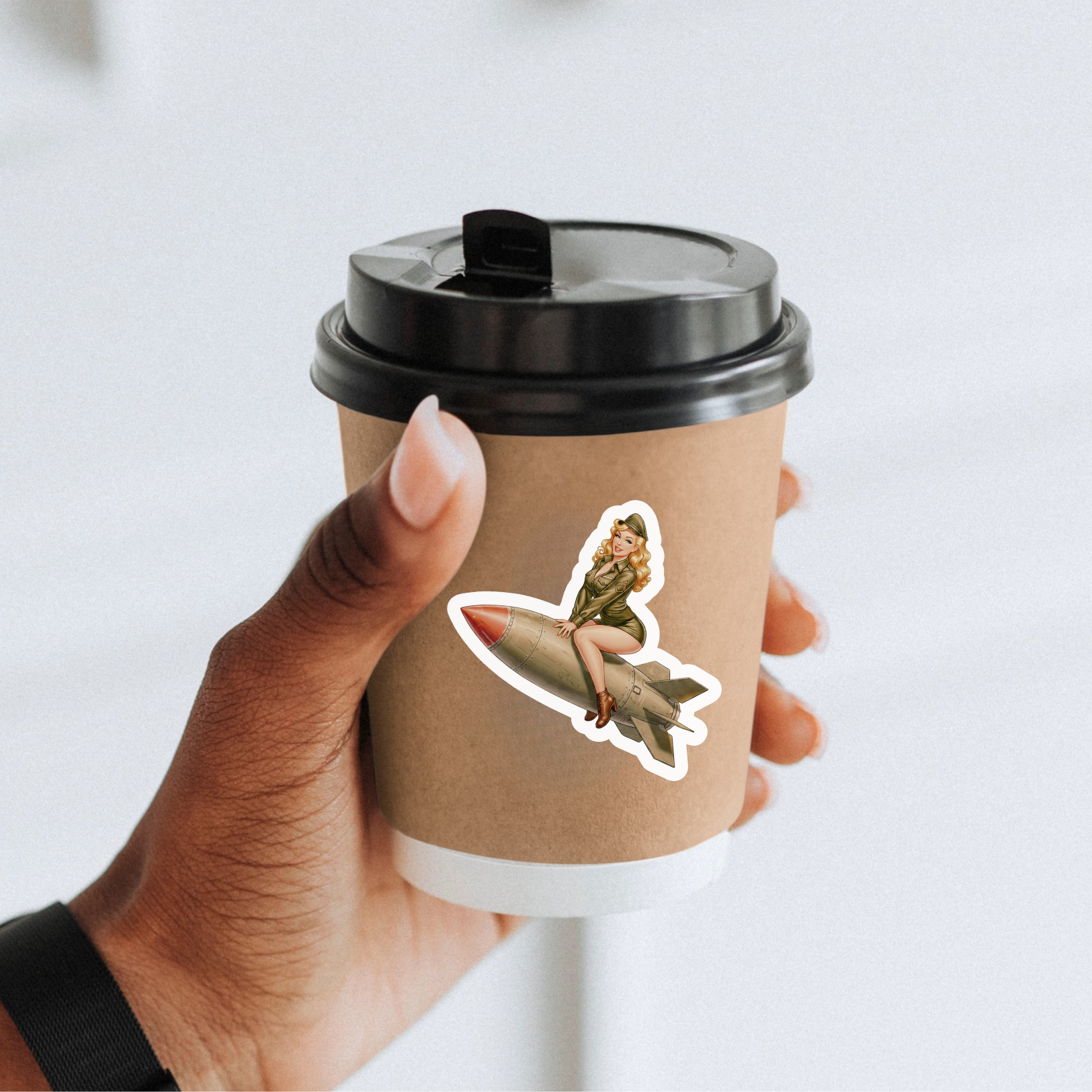 Hand holding a coffee cup with a sticker of a woman on a bomb, against a light background